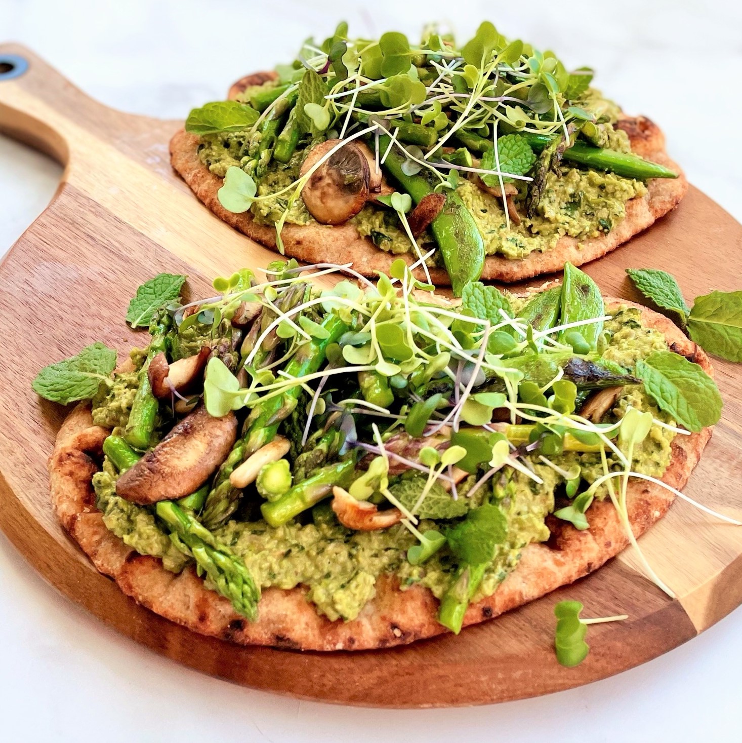 two spring green flatbreads with edamame pesto on round paddle board