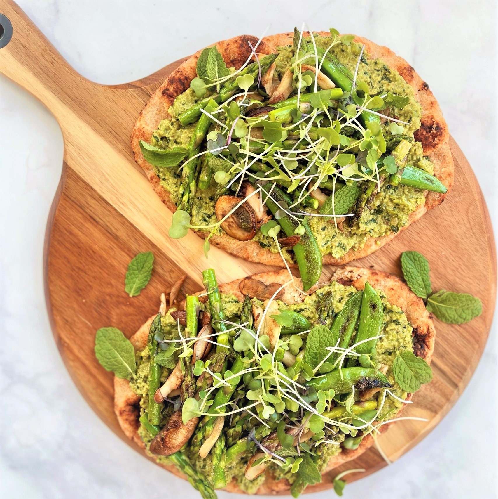 overhead view of spring green flatbread with edamame pesto on wooden paddle cutting board