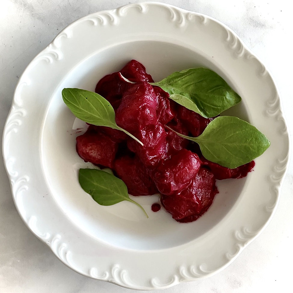 white bowl of gnocchi tossed with fuchsia fun sauce and garnished with fresh basil leaves