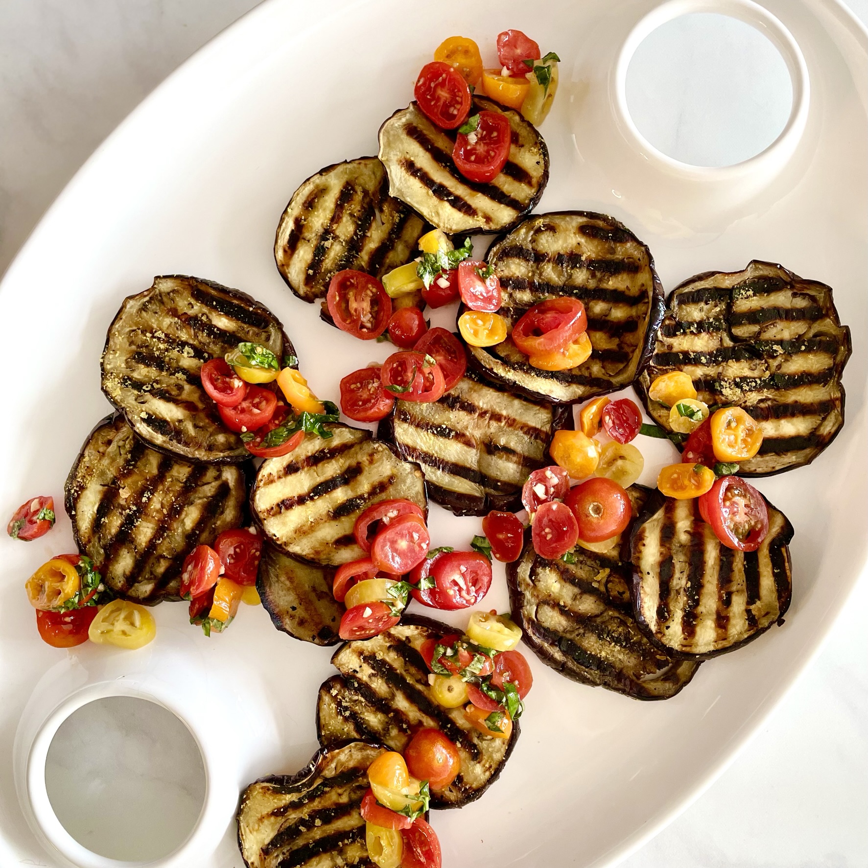 white platter of grilled eggplant topped with tomato-basil salsa