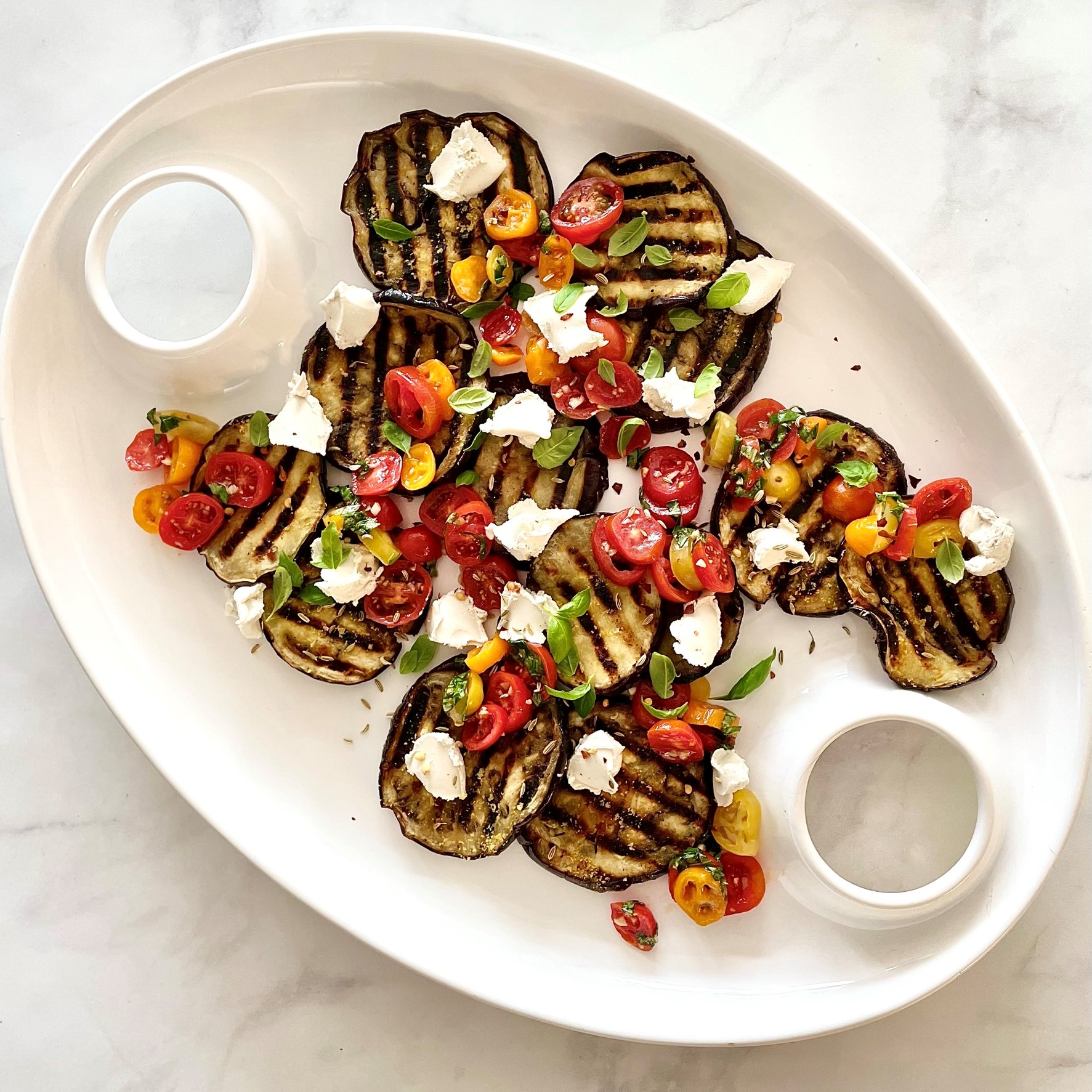 large white platter of grilled eggplant carpaccio with tomato-basil salsa & treenut cheese on white marble