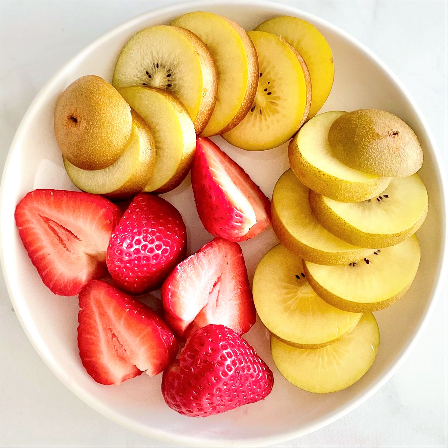 white plate with sliced golden kiwi and halved strawberries