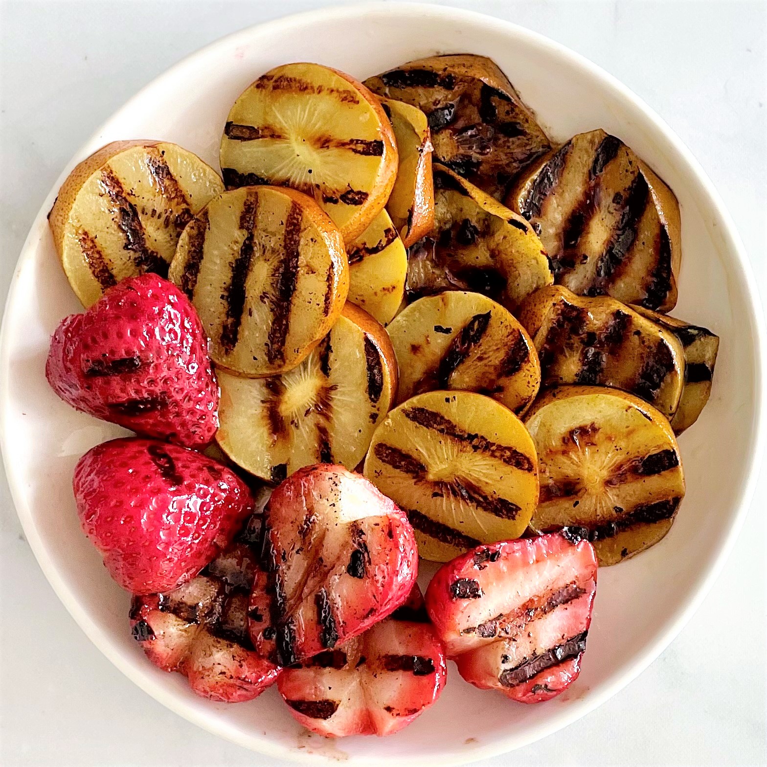 white plate of grilled golden kiwi slices and grilled strawberry halves