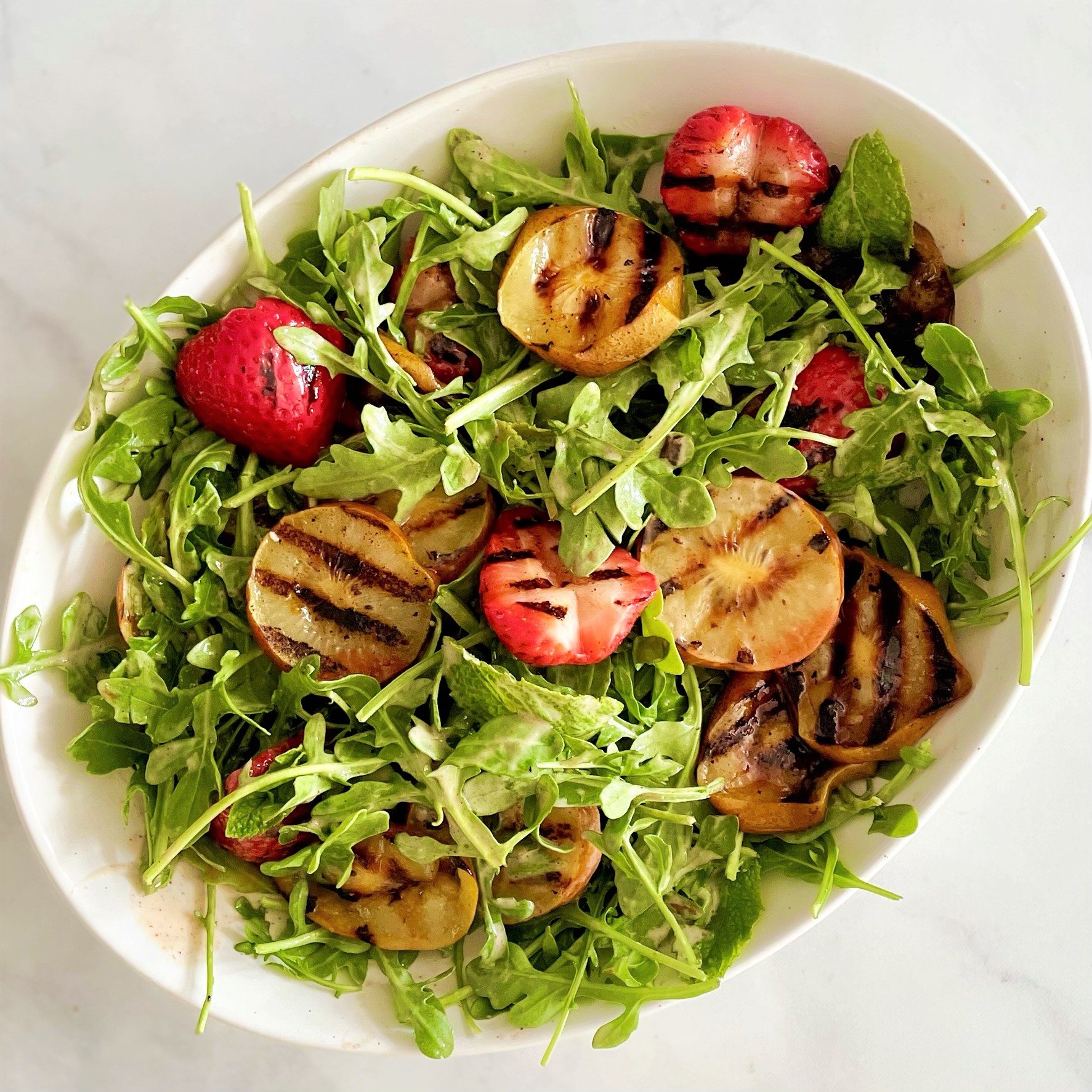 white platter of grilled golden kiwi, strawberry and arugula salad before topping
