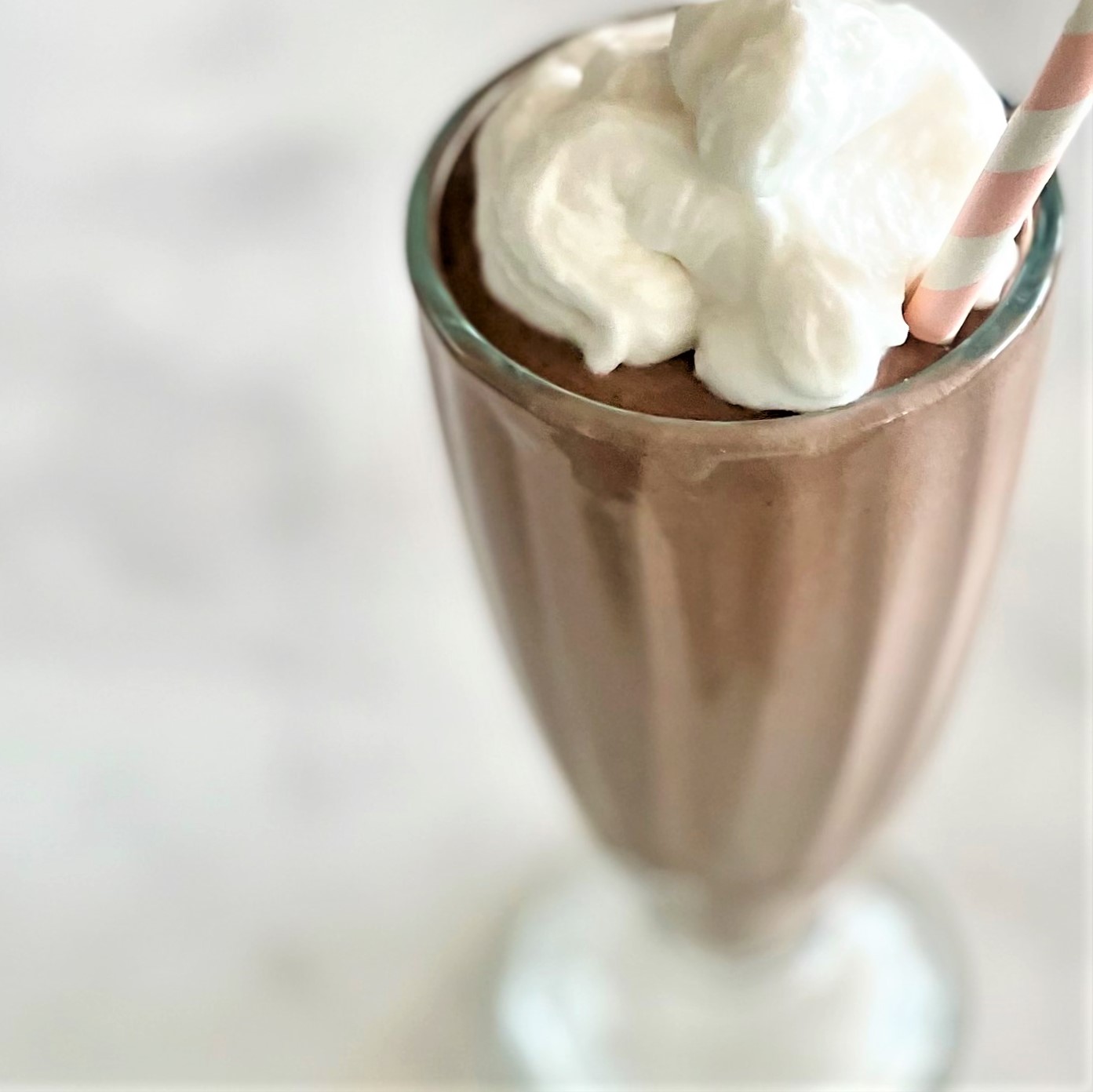 Close-up of Overnight Creamy Cashew Chocolate Shake with coconut whipped cream and a compostable pink and white straw