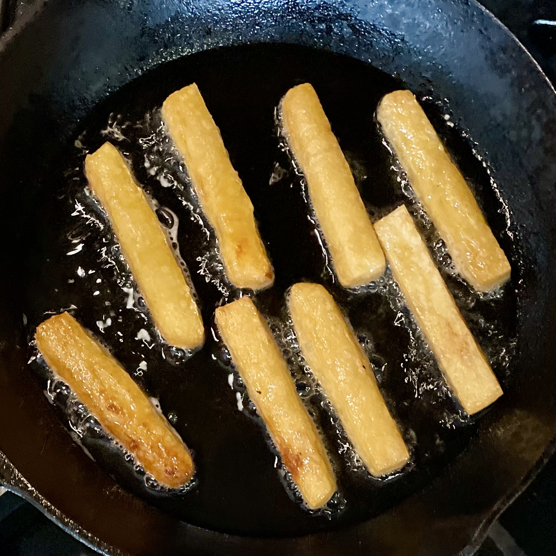 chickpea fries being fried in oil in a cast iron skillet