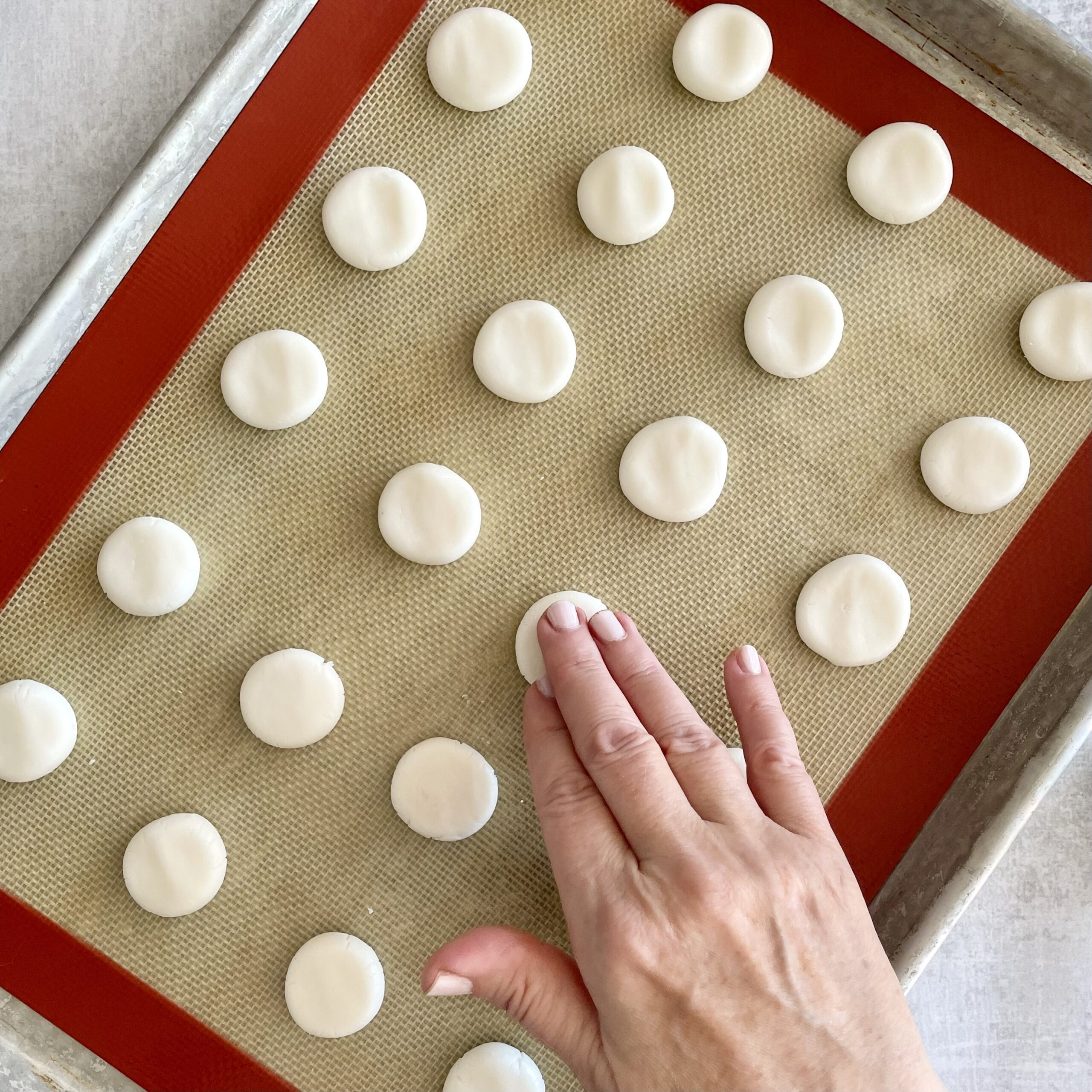 patting white cream filling balls into disks on a silpat lined baking sheet for making dark chocolate mint cream candies