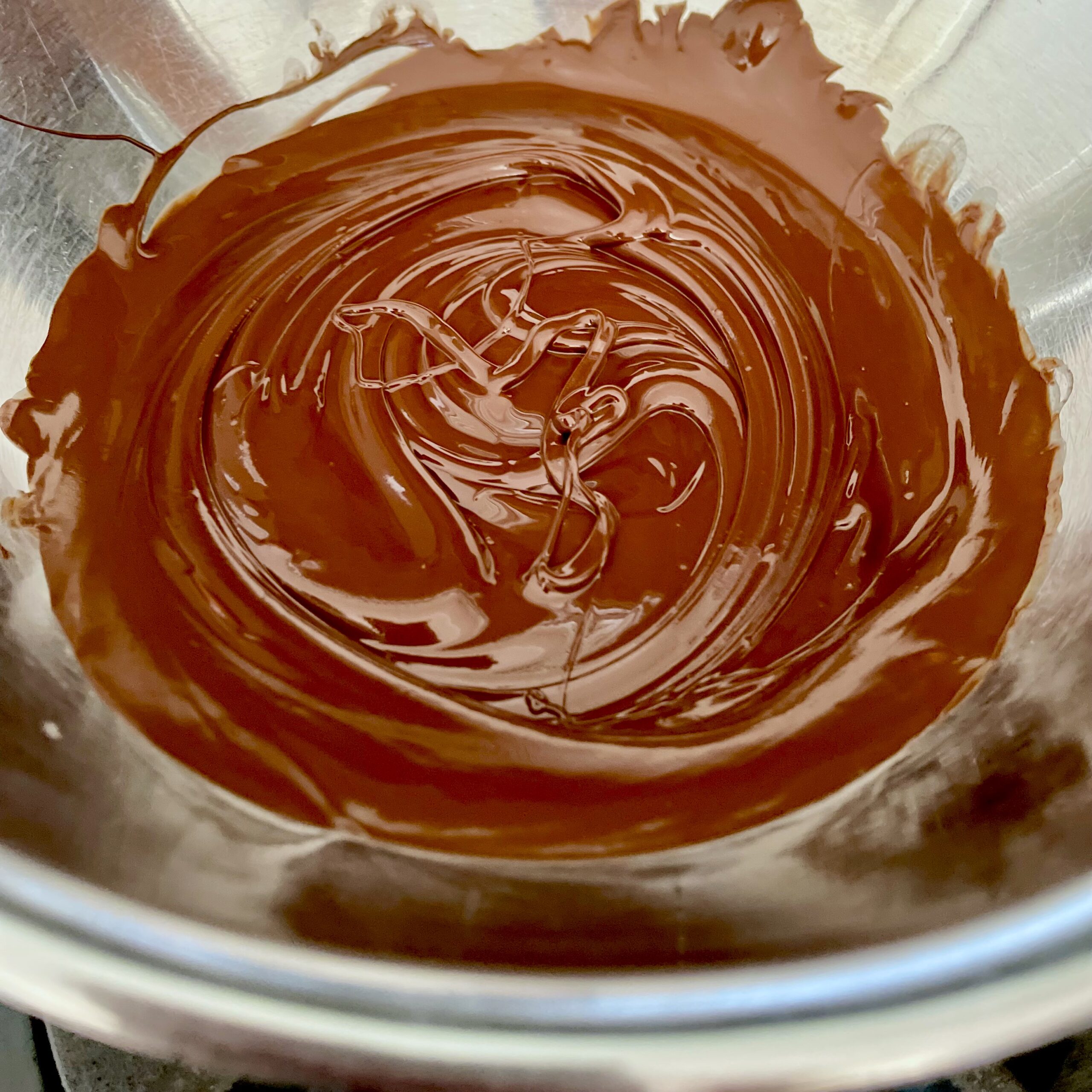 Melted dark chocolate in stainless steel bowl for making dark chocolate mint cream candies 