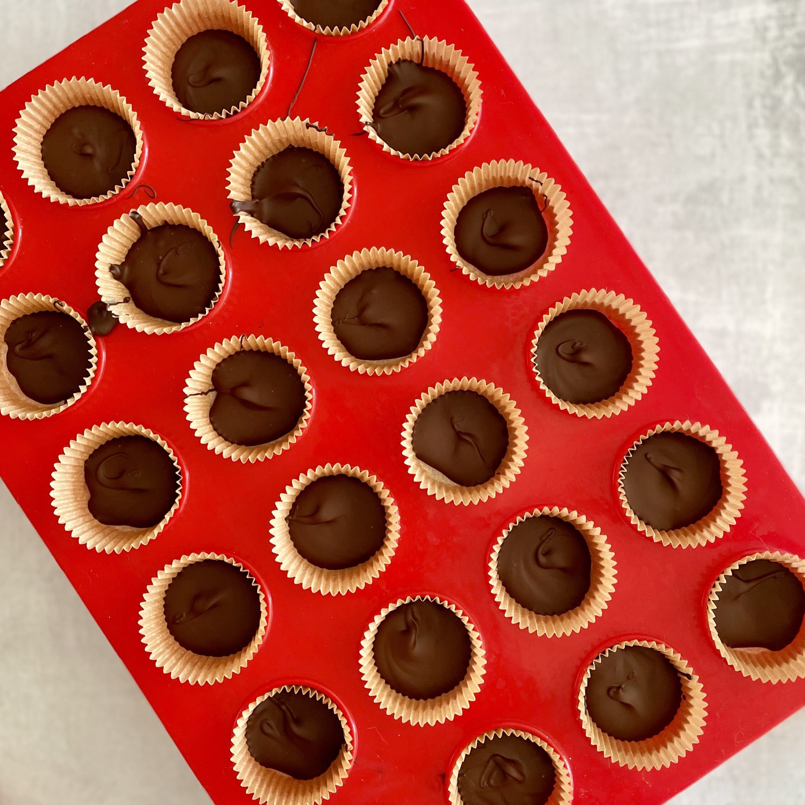 process shot of red mini muffin tin with brown liners filled wih dark chocolate
