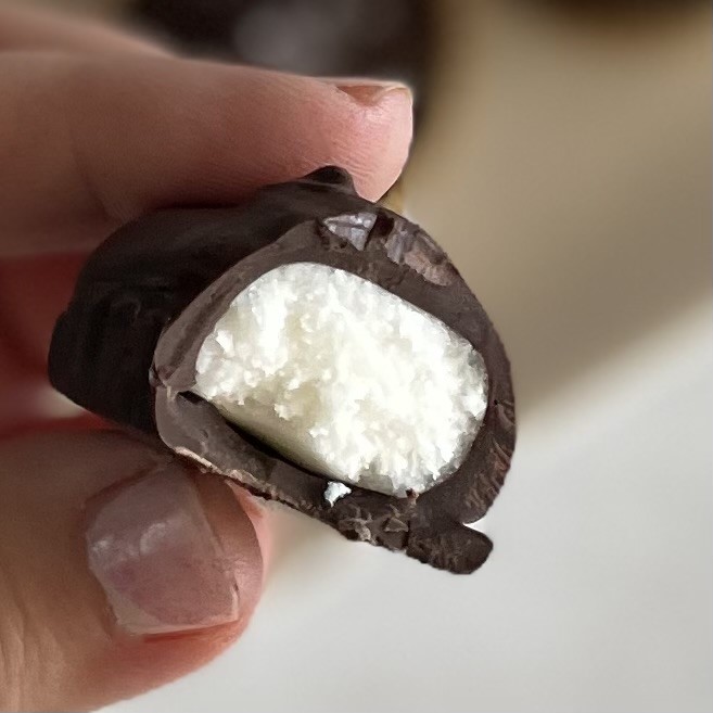 Closeup of holding a half eaten dark chocolate mint cream candy with white cream filling