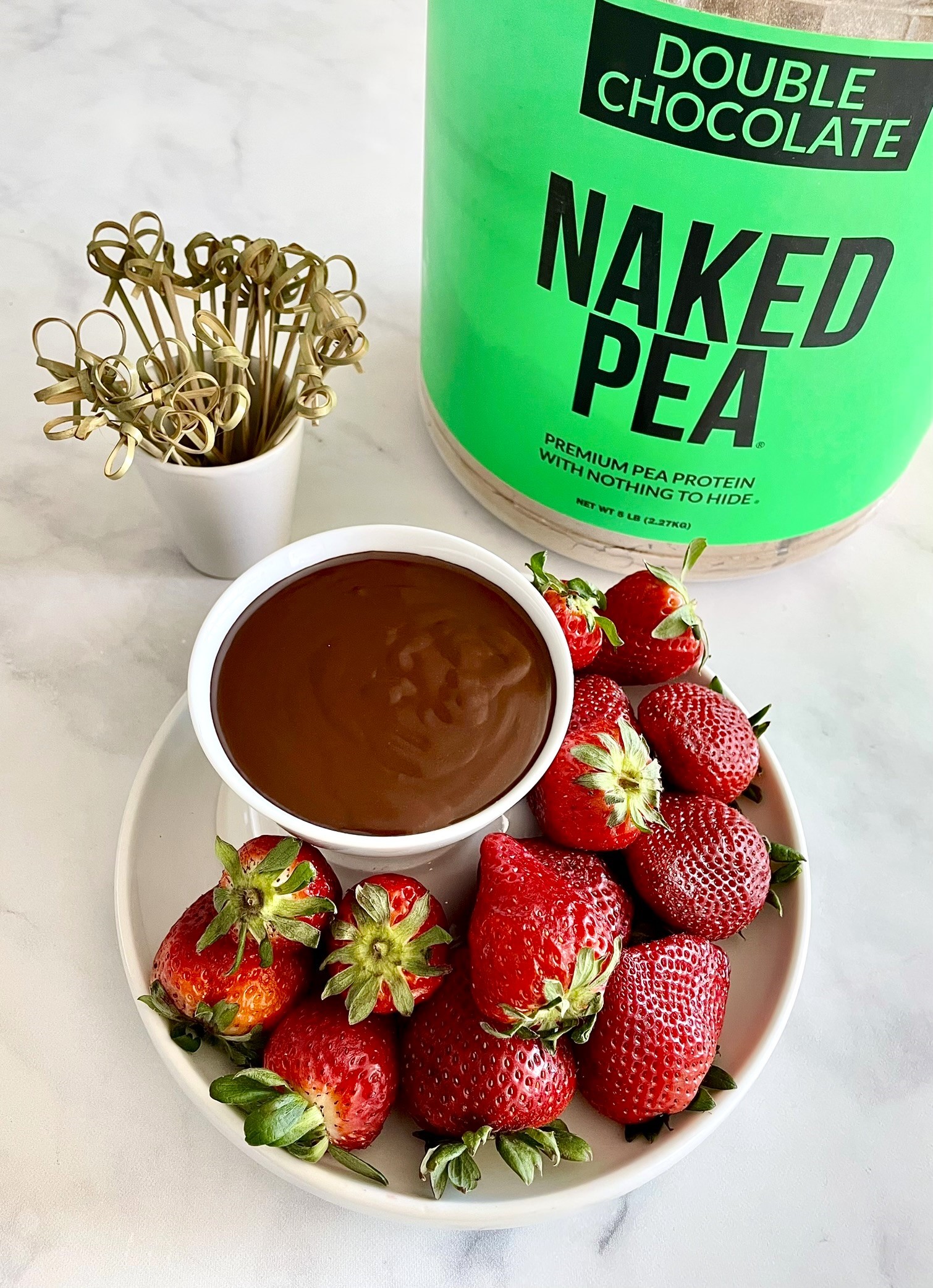 PLate of strawberries with chocolate sauce with Double Chocolate Naked Pea protein powder jar in background