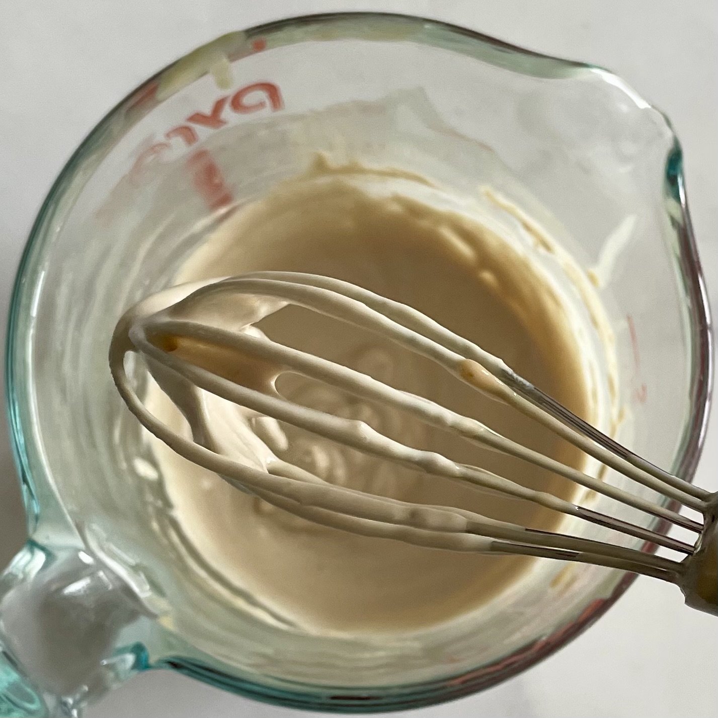 lemony-tahini sauce with a whisk in a glass liquid measuring cup