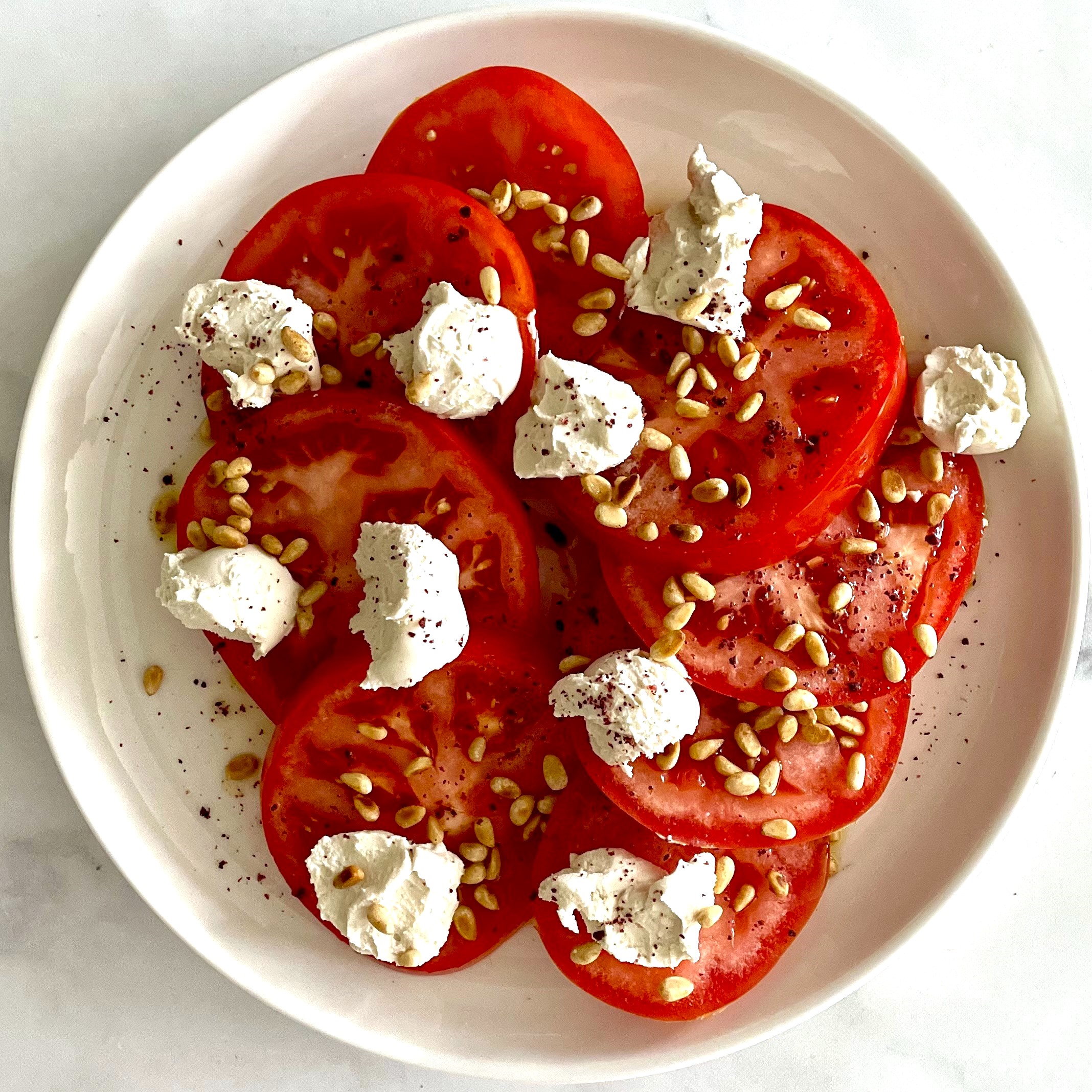 plate of tomato slices with cashew cheese and pine nuts