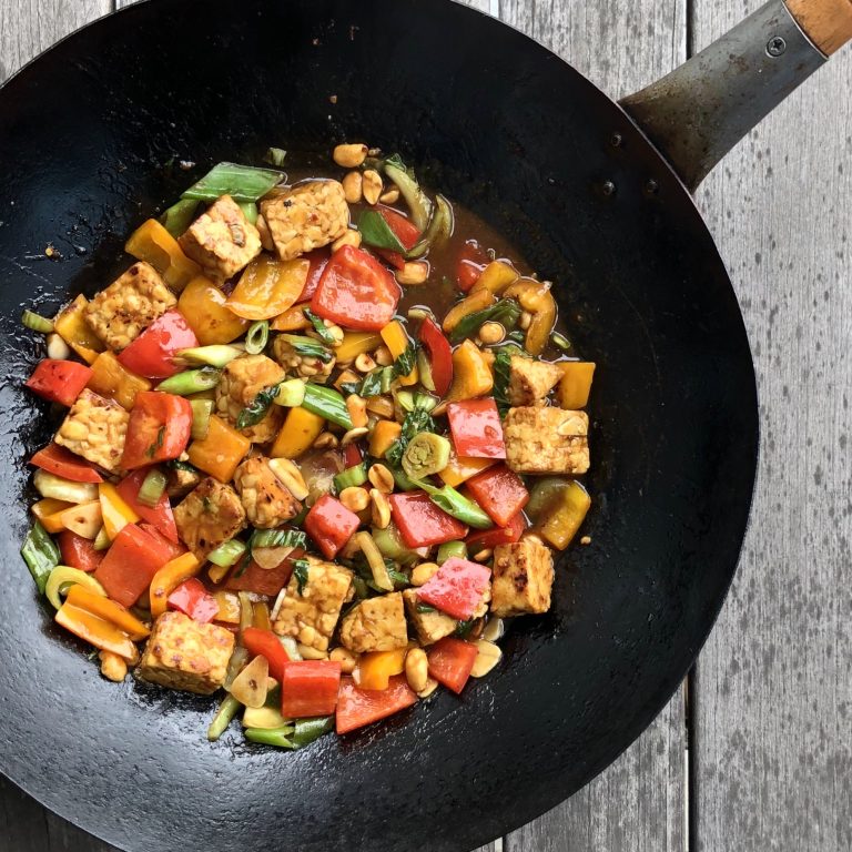 kung pao tempeh stir-fry in wok on wooden table