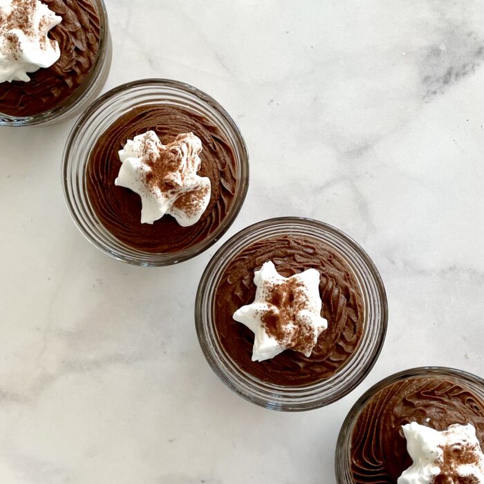 four dessert dishes with no-cook plant-based cocoa mousse topped with coconut whipped cream and dusted with cocoa