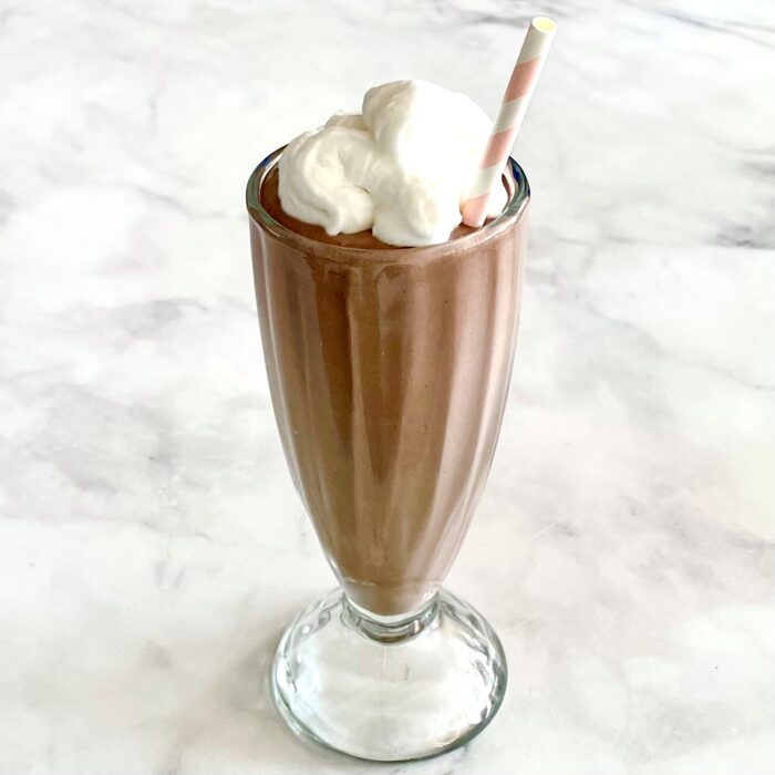 Overnight Creamy Cashew Chocolate Shake with coconut whipped cream and a compostable pink and white straw