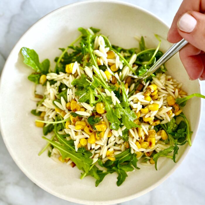 pan-charred corn, orzo & greens salad in white bowl with fork
